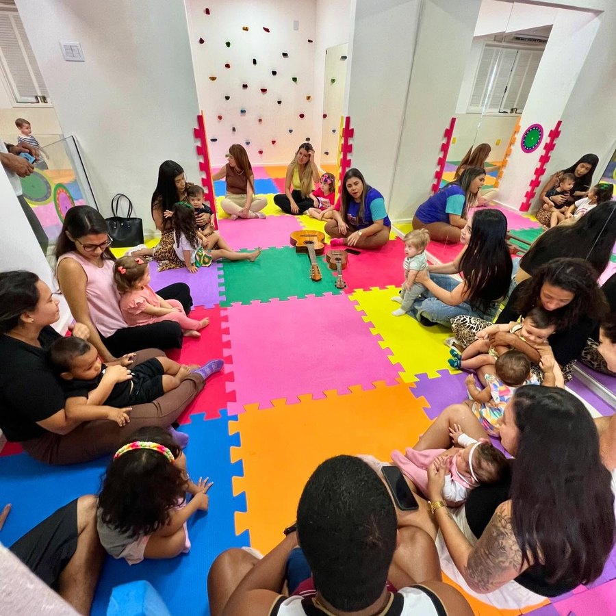 Turma de bebês e responsáveis em roda de música no tatame colorido da Baby Gym Volta Redonda